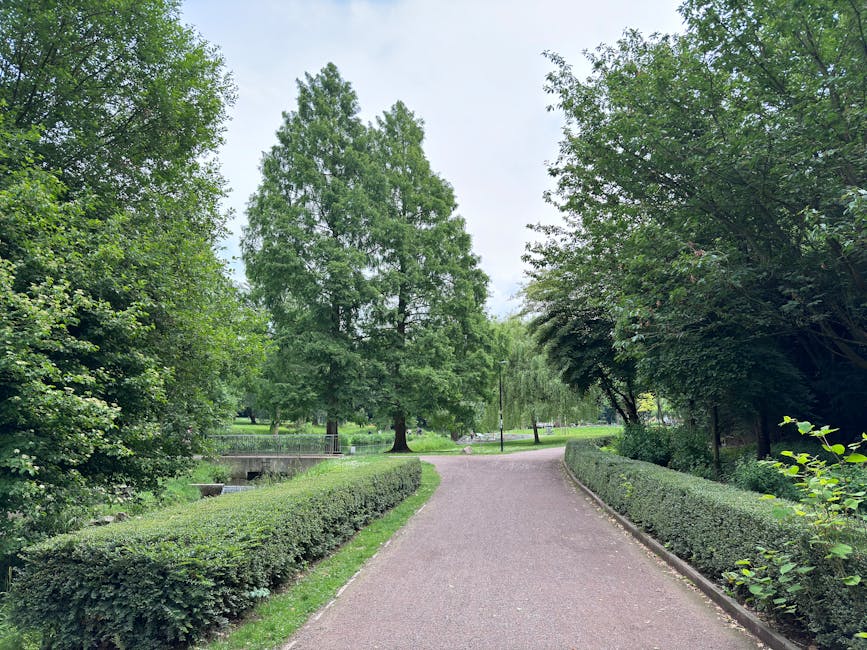 A well-maintained garden featuring vibrant flower beds with blooming pink and white flowers arranged in curved borders, surrounded by lush green grass. In the foreground, there are two black plastic b